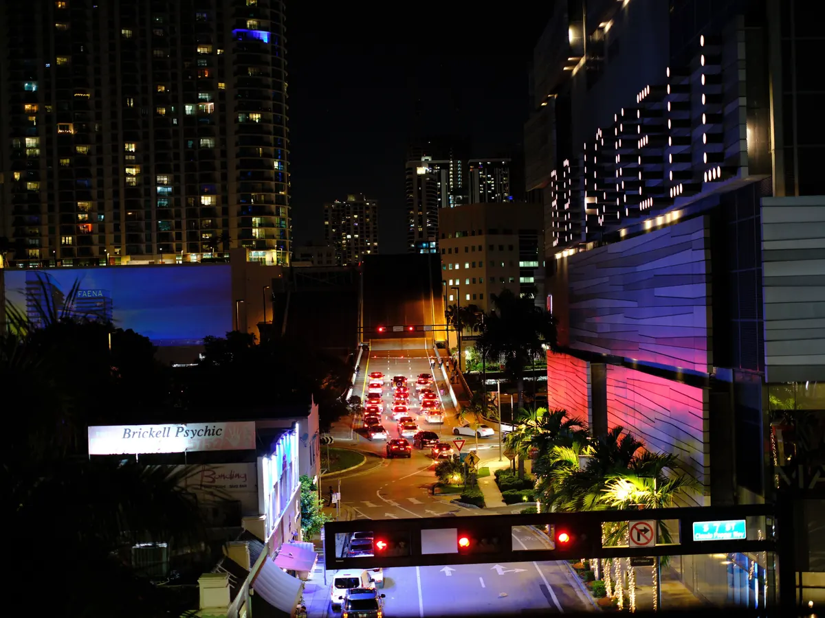 Brickell at night: traffic lights and a line of red tail lights leading to a drawbridge, between illuminated high-rise towers