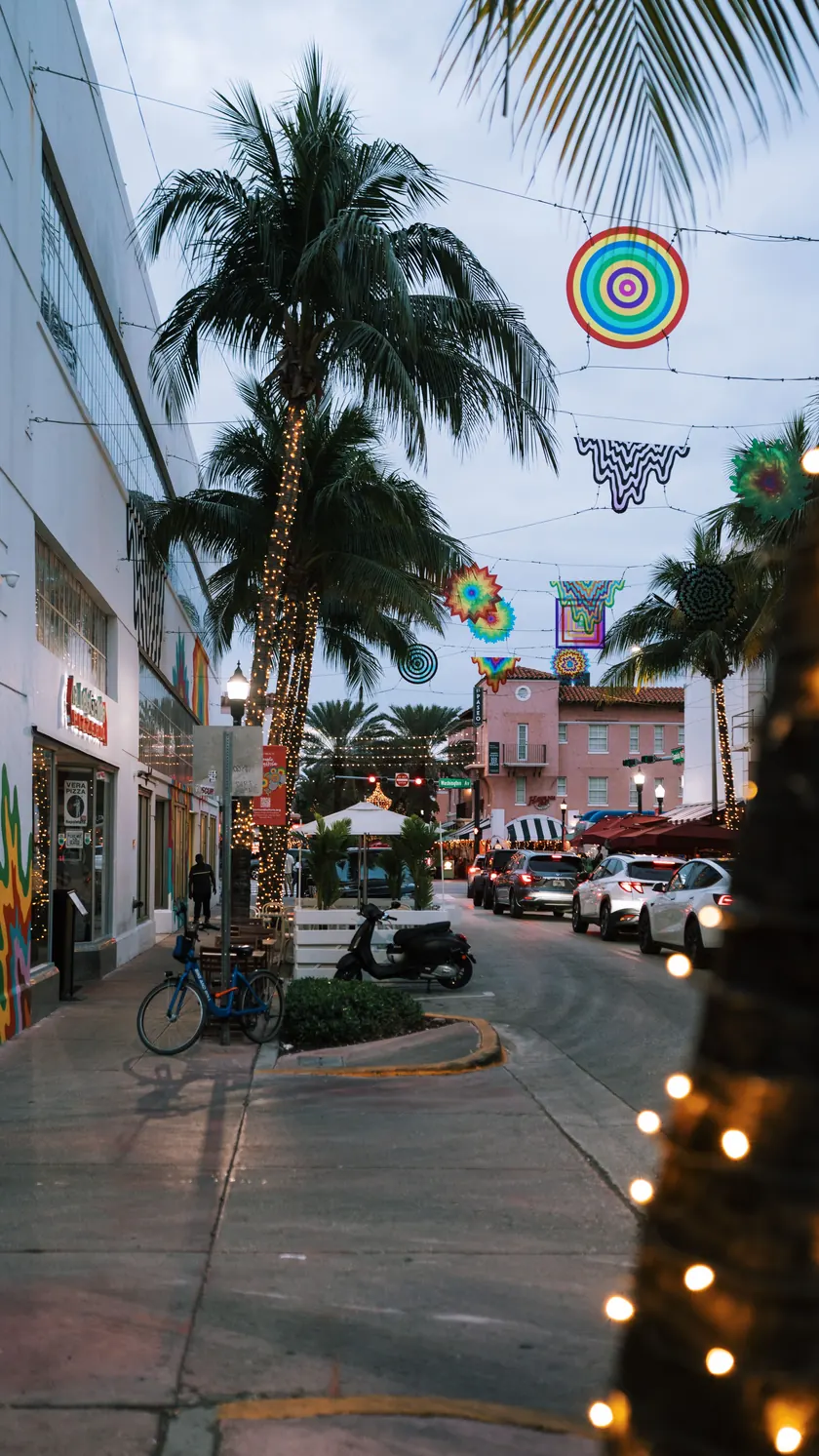 Española Way in South Beach at dusk, with palm trees wrapped in string lights and colorful art hanging over the street
